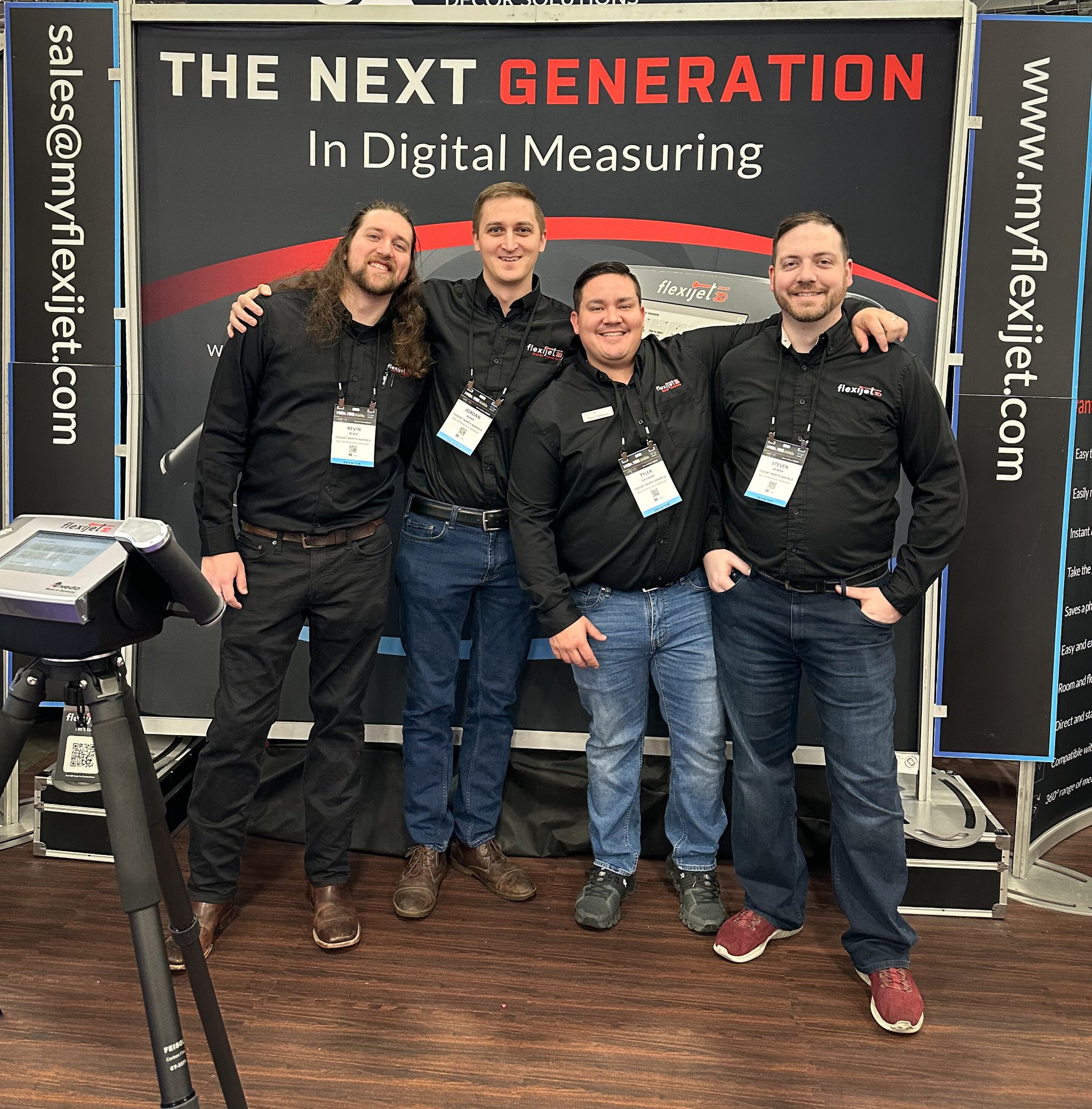 Photo of Flexijet Training and Support, Measurement Expert Team, stood in a group, smiling happy team - Kevin, Jordan, Kyle, Steven exhibiting at an event on Flexijet trade show stand.